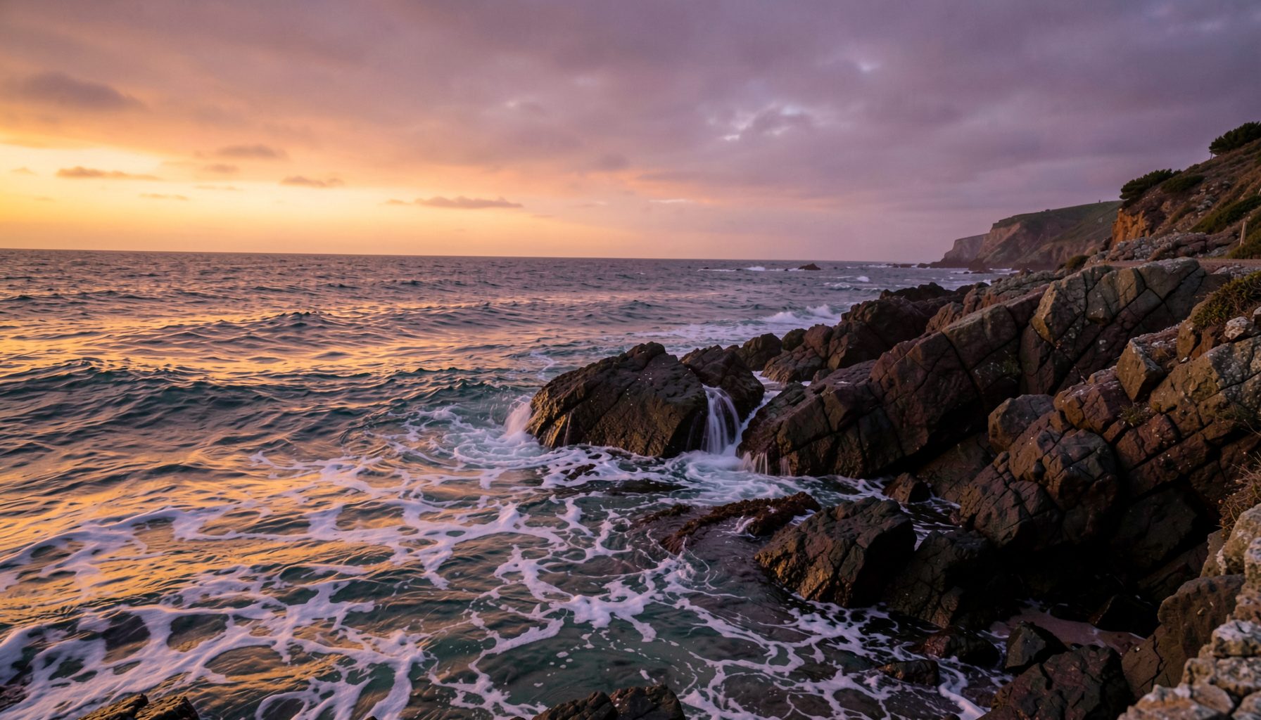 Vue atmosphérique d'une côte rocheuse au crépuscule, vagues douces s'écrasant sur les rochers, tons ambrés et mauves dans le ciel, ambiance calme et contemplative
